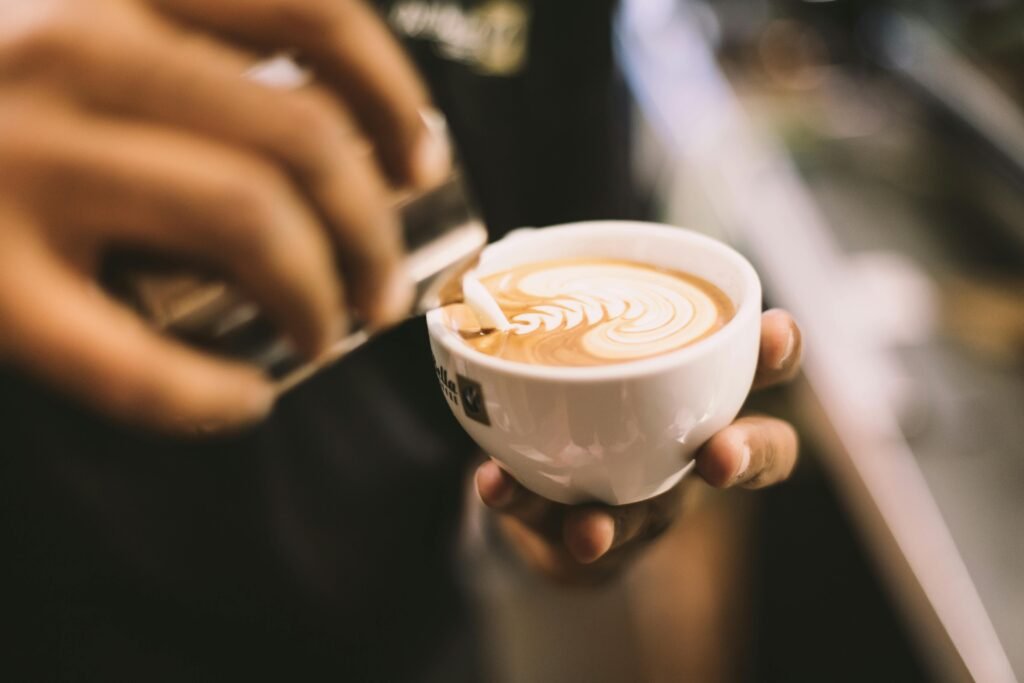 Close-up of a barista pouring milk creating intricate latte art in a coffee cup, indoors.